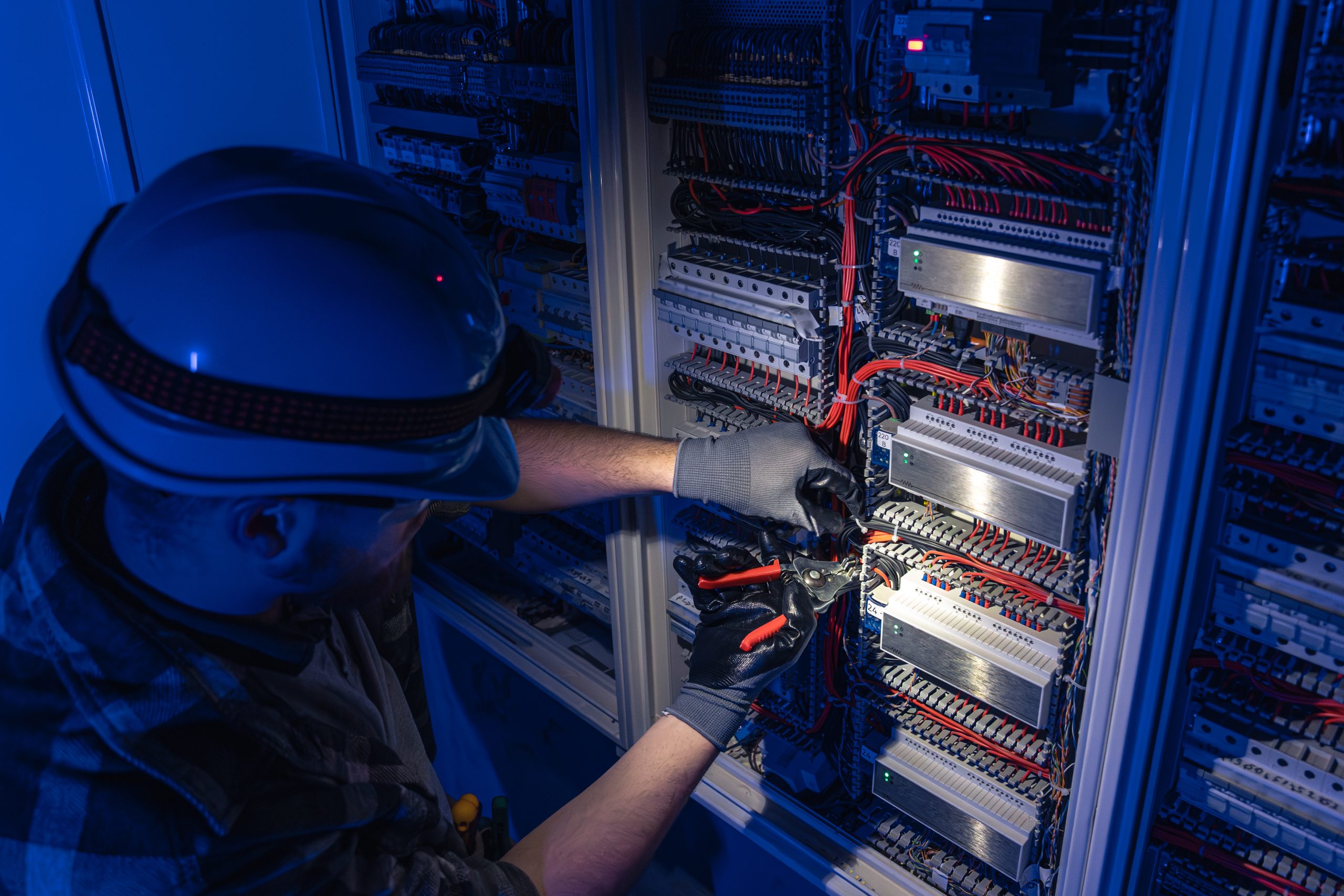 Male electrician working in switchboard with electrical connecting cable. Young adult electrical engineer in special clothes with flashlight on helmet in dark room with emergency lights in background. SSUCv3H4sIAAAAAAAAA41Py26DMBD8lz0byeC2IfxK1IOxF7BicGSvG0WIf+8aiHqtT7sz63ms4Cx00Ch1VRclK2NqWdU1DlXb1G31oeTQWDMY1AgCrCaErlaqlV9KNtfPVl0kPwG9Ts5At4LzPieKmlxYoGMm4mIx7iNaRyE67XnbBCTSlBMm/sabYe2R2X1/693WgnNANk+5L8Mm/ol9C9AjLuZV9LcSxKPe7W5M3Z+EcT69A00lIouEvFB8HUI+hIfuPTcetE8oYNIp8YE9Af74iM64ZTwbcPEwH/MSqDjteSiYu7On1VF6cowWnxXywwdt0Z507mdH9F4j/jh8/l1v2/YLkX0rhrIBAAA=